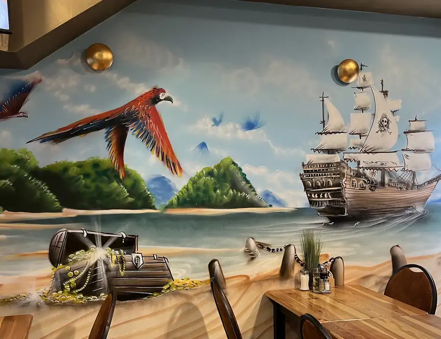 Mural z żaglowcem i papugą nad stolikami